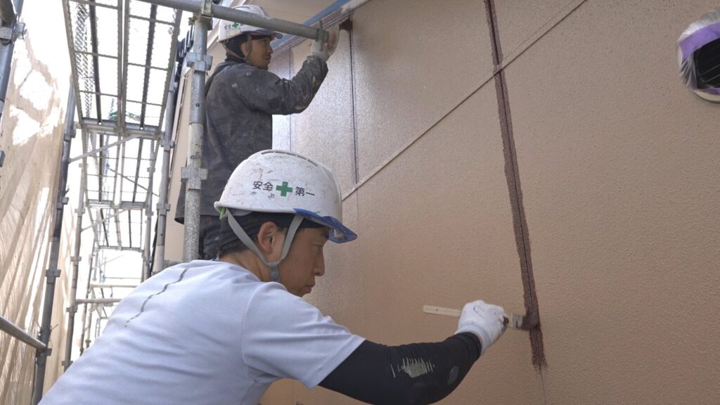 足場の上で外壁を塗る職人