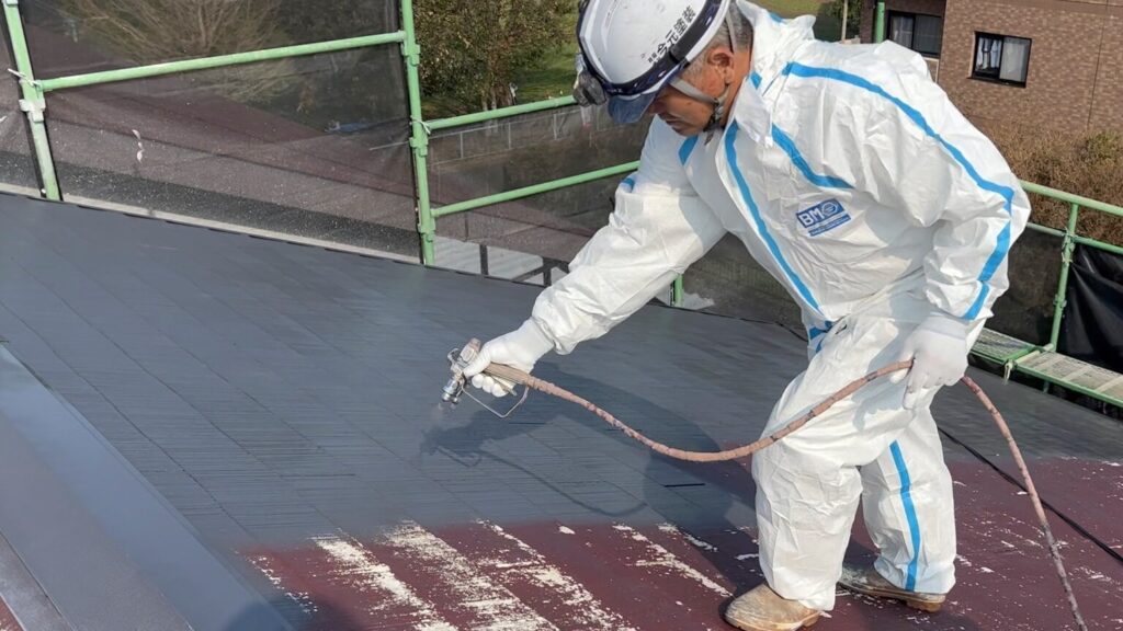 屋根をスプレーで塗装する職人