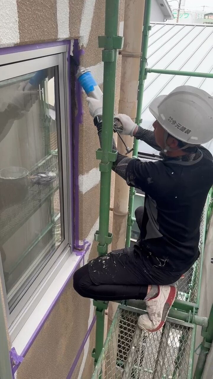 足場の上で窓まわりのすき間を埋める職人